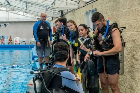 Divemaster acompañando a instructor en una clase en pileta con 5 alumnos